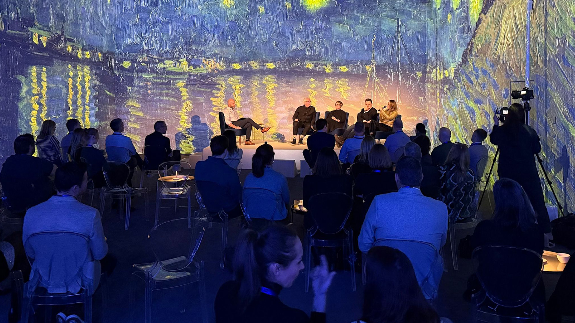 Panel discussion on stage with a crowd of people and an immersive digital background