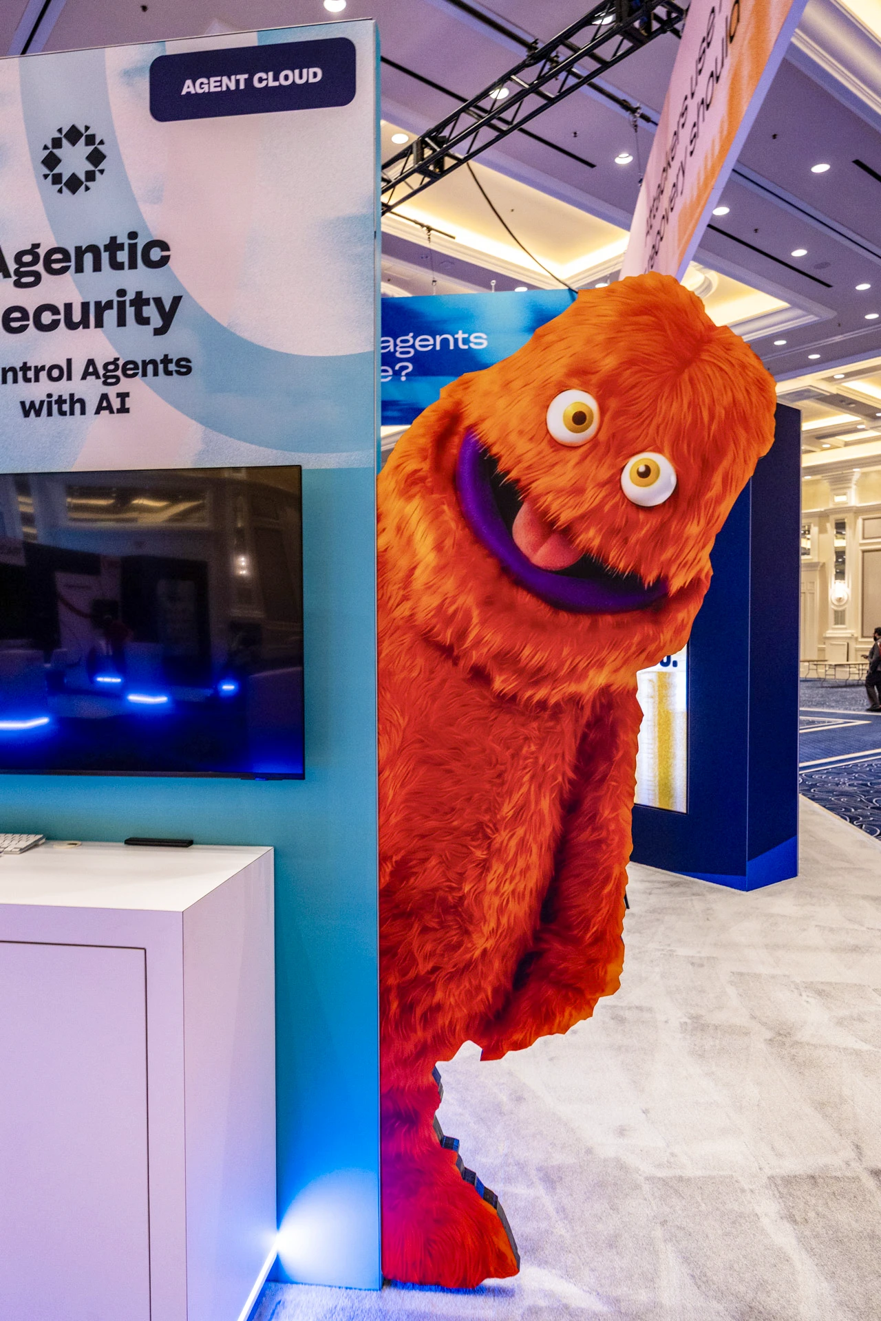 Orange mascot character beside a branded technology exhibition stand at Rubrik Forward 2026